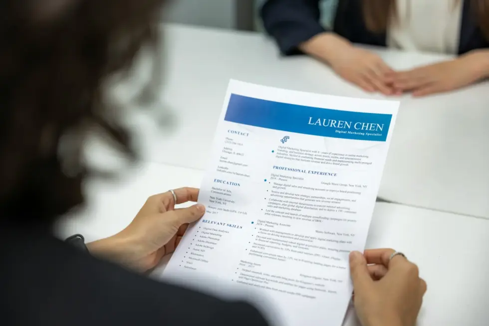 Curriculum vitae di una specialista in marketing digitale, tenuto in mano durante un colloquio di lavoro, con particolare attenzione alle sezioni dedicate ai contatti e all’esperienza.