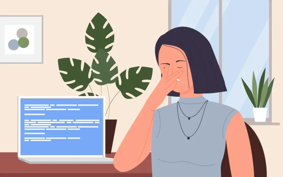 Una donna con i capelli corti è seduta a una scrivania, frustrata, si copre il viso mentre guarda un computer portatile che mostra del codice. Accanto a lei ci sono delle piante verdi.