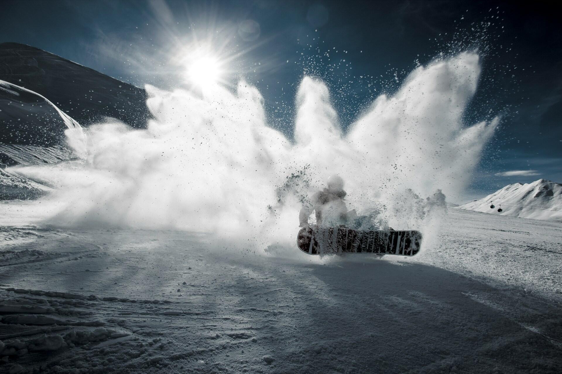 A snowboarder descends the side of a mountain, creating a cloud of snow.