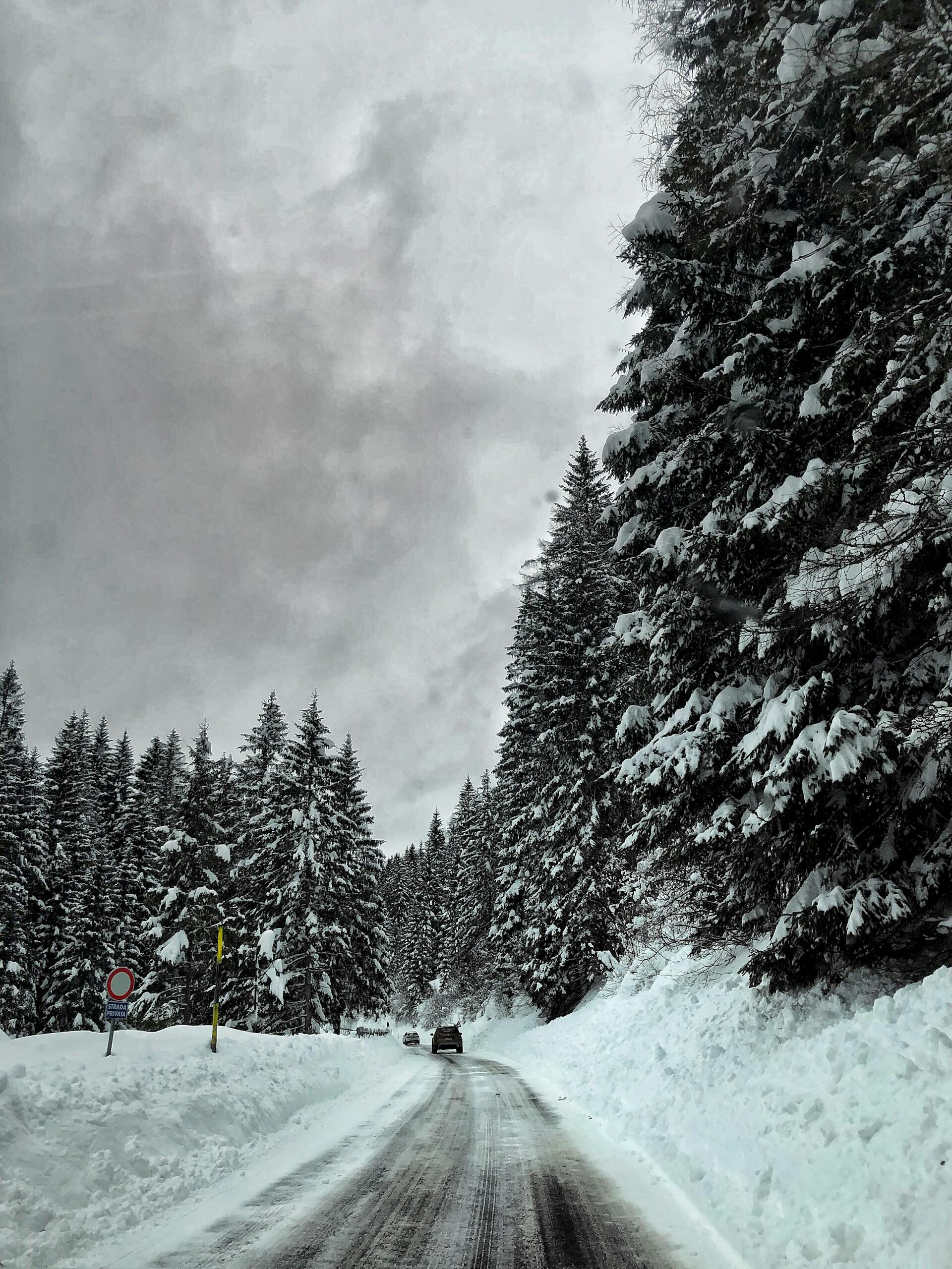 Snow-covered mountain road with a car in the distance.